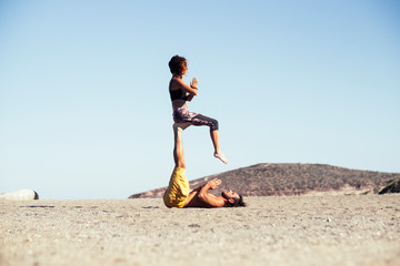 couple of two adults in relationship or friendship doing acro yoga together - man holding with his legs a woman while she's sit