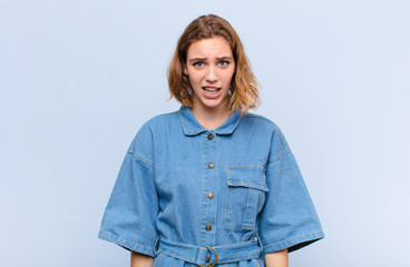 Wall Mural - young blonde woman looking shocked, angry, annoyed or disappointed, open mouthed and furious against flat color wall