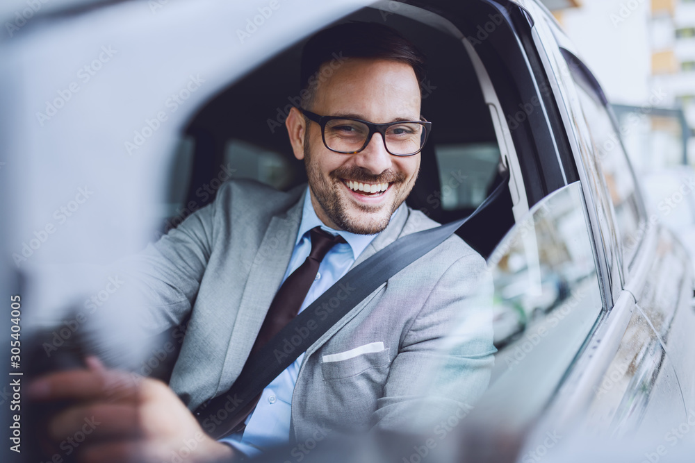 Cheerful caucasian businessman driving himself to work. Hands are on steering wheel. - obrazy, fototapety, plakaty 