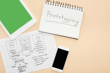 top view of gadgets near website design template and notebook with prototyping lettering on beige background