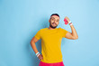 © master1305 - Young caucasian man in bright clothes training on blue background Concept of sport, human emotions, facial expression, healthy lifestyle, youth, sales. Training with the colorful weights. Copyspace.