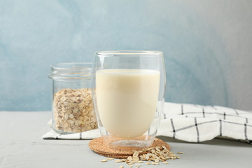 Glass of oat milk, oatmeal seeds, napkin on grey background, space for text