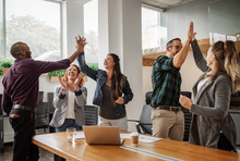 Diverse Business Team Celebrating And Giving High Fives During Boardroom Meeting
