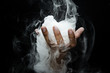 Hand smoke from dry ice in a bowl, black background.