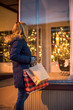 christmas shopper holding bags looking in store window at night