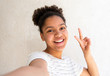 © mimagephotos - Close up happy young african american girl taking selfie against white background with peace hand sign