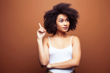 pretty young african american woman with curly hair posing cheerful gesturing on brown background, lifestyle people concept