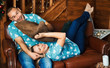 Happy emotional couple have fun together on the couch. The man is sitting. The woman is lying. The husband is trying to strangle a woman with a pillow.