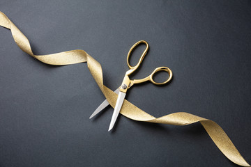 Grand opening. Gold scissors cutting gold satin ribbon, black background