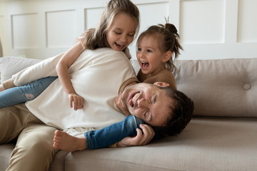 Funny young father playing with cute little children on sofa