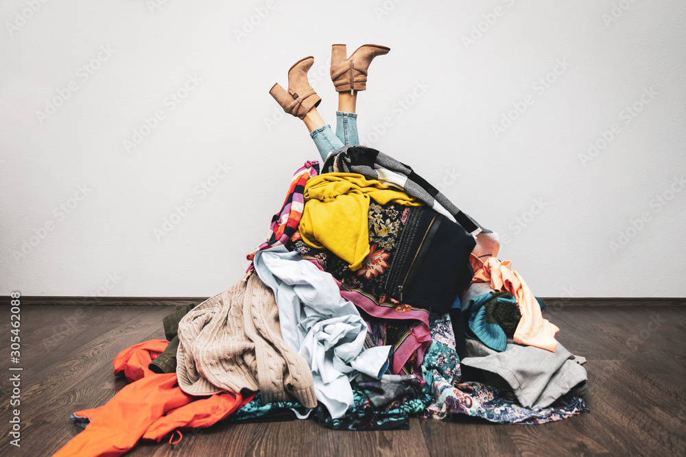 woman legs out of a pile of clothes on the floor. shopping addiction concept - obrazy, fototapety, plakaty 