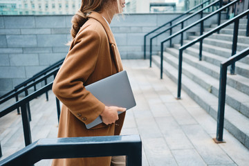 close up young businesswoman in coat with laptop on street