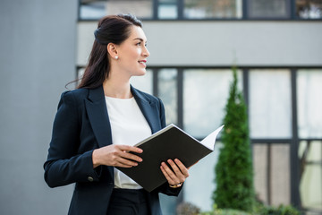 happy and attractive diplomat holding folder near building outside