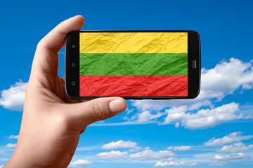 Lithuania flag on the phone screen. Smartphone in hand shows a flag on a background of the sky with clouds.