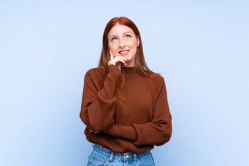 Young redhead woman over isolated blue background thinking an idea while looking up