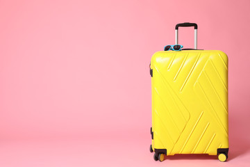 Yellow suitcase with sunglasses on pink background. Space for text