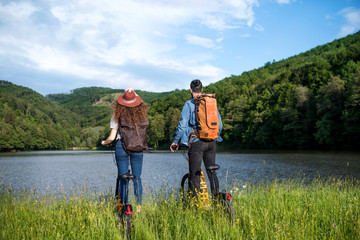 Wall Mural - rear view of young tourist couple with electric scooters in nature, standing by lake.