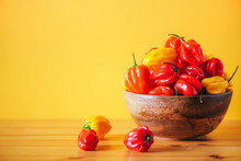 Yellow And Red Scotch Bonnet Chili Peppers In Wooden Bowl Over Orange Background. Copy Space.