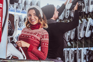 Wall Mural - Young couple standing near rack with many pairs of skates, choosing his size