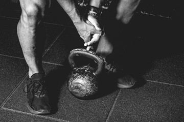 Strong fit muscular man with muscles holding heavy kettle bell with his hand on the gym floor prepared for cross strength and conditioning training and workout black and white