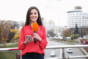 Canvas Print - Young female journalist with microphone and smartphone working on city street. Space for text