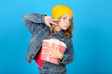 Wall Mural - Young girl holding bucket with popcorn on blue background