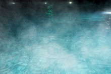 Pure Clear Water In The Thermal Pool. Hot Water Flows, And Fog Rises Above The Pool, The Pool Itself Is Illuminated By Lanterns. Blue Water, Beautiful Background.