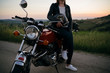 © Westend61 - Crop shot of young woman with vintage motorbike on country road at sunset, Tuscany, Italy