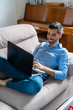 © Westend61 - Smiling young man sitting on the couch at home using laptop