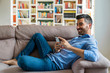 © Westend61 - Smiling young man lying on the couch at home using smartphone