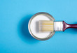 Open can with white paint and brush on blue background, top view. Space for text
