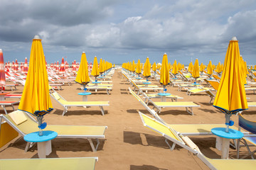 Canvas Print - Sun umbrellas and deck chairs on sandy beach on cloudy day. Rimini resort beach, Italy