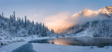 Fototapeta Natura - Sunrise in winter mountains. Mountain reflected in ice lake in morning sunlight. Amazing panoramic nature landscape in mountain valley.