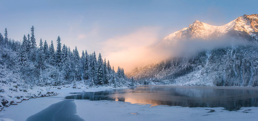 Canvas Print - Sunrise in winter mountains. Mountain reflected in ice lake in morning sunlight. Amazing panoramic nature landscape in mountain valley.
