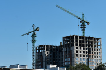 Building site with two cranes on blue sky background with half-constructed house