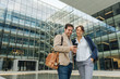 © Hernandez And Sorokina/ADDICTIVE STOCK - Optimistic businesspeople smiling and browsing on mobile phone while standing outside modern building and resting after work