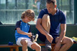 © PHILIPPE DEGROOTE/ADDICTIVE STOCK - Little boy smiling and putting on sneaker while sitting on bench near trainer before workout