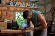 © PHILIPPE DEGROOTE/ADDICTIVE STOCK - Side view of skilled middle aged handyman in overalls using clamp while working with wooden plank in workshop