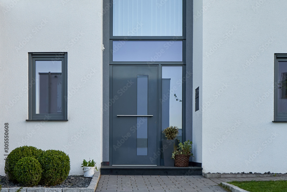 Facade of a modern house with a gray front door and potted flowers. - obrazy, fototapety, plakaty 
