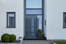 Facade Of A Modern House With A Gray Front Door And Potted Flowers.