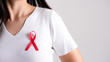 Closeup of red badge ribbon on woman chest to support AIDS Day. Healthcare, medicine and AIDS awareness concept.