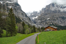 Quiet Country Road Passes Dramatic Swiss Alpine Mountain Landscape With A Farm Hut Surrounded By Lush Wildflower Meadows On The Way Down The Grosse Scheidegg Pass Towards Grindelwald