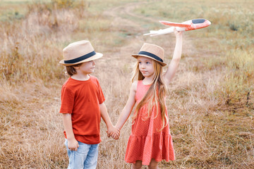 Little children - daughter and son is playing and dreaming of flying. Child care. Cute children - daughter and son playing with toy airplane in the meadow in vintage color tone.