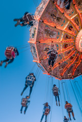 Wall Mural - Amusement park motion blurred riders on retro vintage tilting swing against clear blue sky.