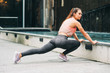© annanahabed - Outdoor portrait of young beautiful fit woman stretching legs, wearing fashionable activewear, athlete model posing in urban background, sport fashion