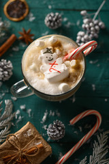 Wall Mural - Christmas and New Year. Marshmallow snowman in hot latte in a mug. Vertical composition on a green background.