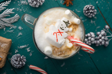 Wall Mural - Christmas composition, mug with hot chocolate with melted snowman marshmallows and caramel. horizontal frame over green background