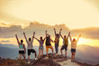 canvas print picture - Happy friends stands with raised arms against sunet mountains