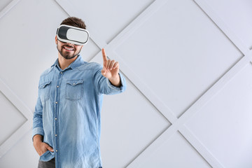 Wall Mural - Young man with virtual reality glasses on grey background