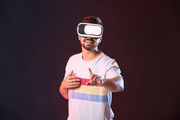 Wall Mural - Young man with virtual reality glasses on dark background